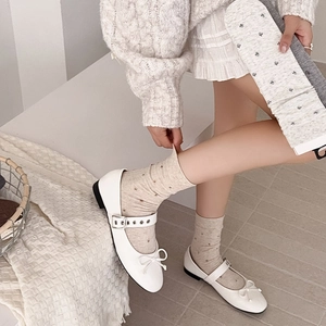 Close-up of white Mary Jane flat shoes paired with polka dot knit crew socks on feet