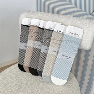 Close-up of six pairs of striped crew socks in neutral tones on a textured white surface