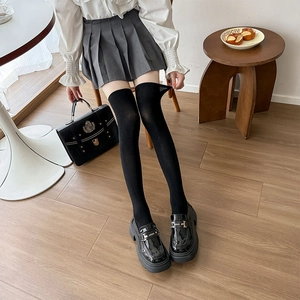 Detail of black over-the-knee socks paired with platform loafers and a gray pleated skirt