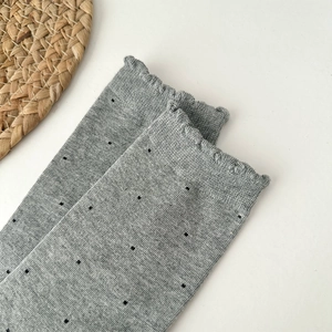 Detail shot of light grey knit socks with black polka dots and wavy ruffle cuffs