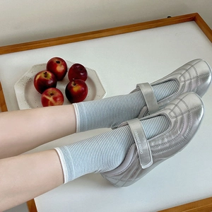 Detail of silver Mary Jane flat shoes featuring a logo strap with striped socks