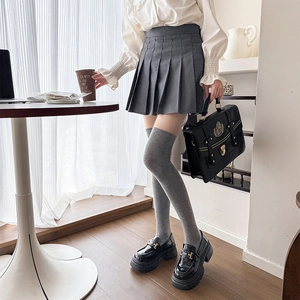 Detail of grey over-the-knee socks paired with a pleated skirt and black platform loafers