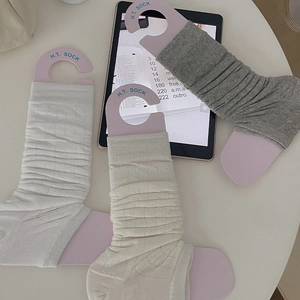 Detail of ribbed knit leg warmers in white, beige, and grey with branded paper tags