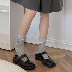 Detail of grey crew sock with bear embroidery paired with black Mary Jane shoes