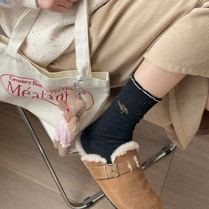 Close-up of black speckled socks with 'cute' embroidery paired with brown suede mules