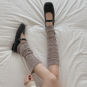 Detail of khaki cable-knit leg warmers paired with grey Mary Jane shoes on white bedding