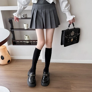 Détail d'une jupe plissée grise assortie à des chaussettes hautes et mocassins noirs