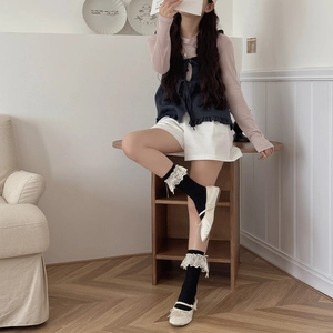 Close-up of black lace-edged knee-high socks with bows and cream Mary Jane shoes