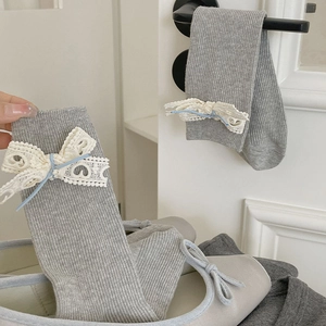 Détail de chaussettes en maille grise avec nœuds en dentelle blanche et rubans bleus