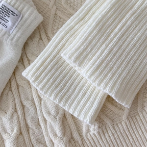 Macro detail of creamy white ribbed knit leg warmer with decorative fabric label text