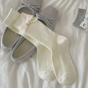 Détail de chaussettes en maille crème avec bordure en dentelle blanche et nœuds roses