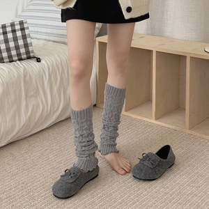 Detail of grey cable-knit leg warmers paired with bow-decorated felt shoes in bedroom