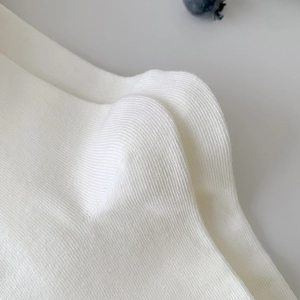 Detail of white rib-knit fabric with soft textures and a decorative blueberry accent