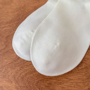 Macro detail of white Lolita socks toe seam and soft knit texture on wood surface