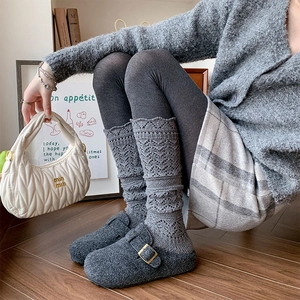 Detailed view of light gray openwork knit leg warmers paired with gray felt clogs