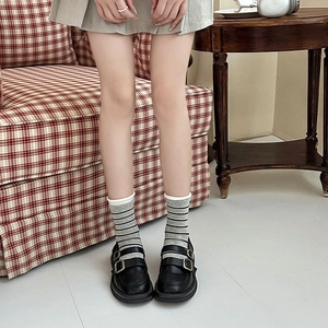 Detail von grau gestreiften Socken kombiniert mit schwarzen Mary-Jane-Schuhen aus Leder