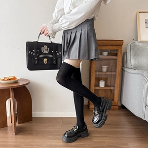 Full view of black over-knee socks with JK pleated skirt and leather loafers in indoor setting