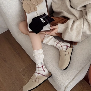 Detail of plaid knit socks and beige clogs featuring a stylish brand woven label