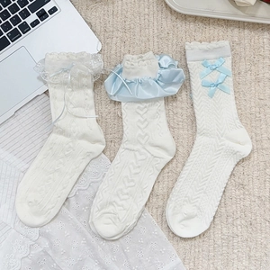 Three pairs of white Lolita style lace trim socks with blue bows on a beige background