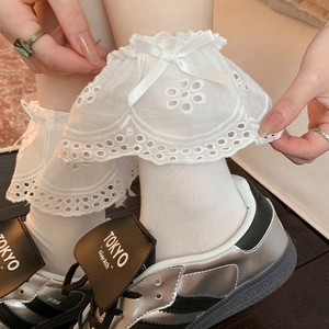 Detail of white lace socks with satin bow, ruffled edges and delicate hollow embroidery