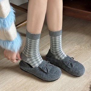 Detail of wool slippers with bow and grey plaid socks on light wood flooring