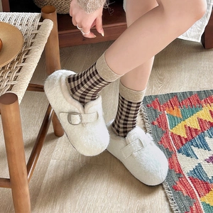Close-up of cream fuzzy mule slippers with adjustable metal buckle and plaid socks