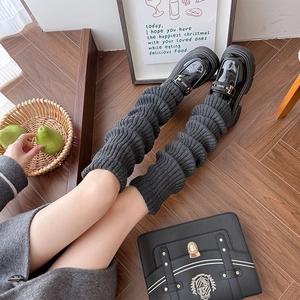 Close-up of dark grey knitted leg warmers styled with black loafers on wooden floor