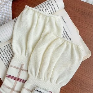 Detailed close-up of cream knit leg warmers with retro plaid trim on a wooden table