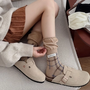 Detail of camel plaid knit slouch socks paired with beige suede mule shoes on a rug