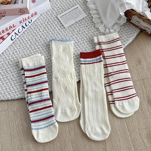 Close-up of four sets of preppy cream cotton socks with red and blue stripes and hearts