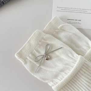 Close-up of white ribbed knit socks with metallic bow and heart pendant detail
