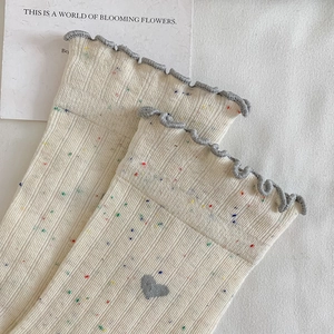 Gros plan de chaussettes en coton ivoire avec bords à volants gris et mouchetures colorées