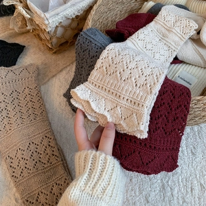 Close-up of cream knit leg warmers with delicate hollow patterns and wavy edges