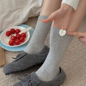 Grey ribbed mid-calf socks with white heart patch worn with dark loafers on a cozy rug