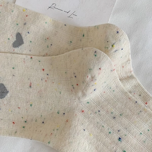 Gros plan de chaussettes en tricot crème avec confettis colorés et motifs de cœurs gris