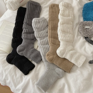 Flat lay of cable knit slouch leg warmers in various colors on a white bed sheet