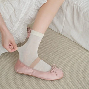 Close-up of pink satin ballet flats with white sheer mid-calf socks being stretched