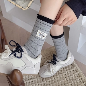 Detail of grey striped crew socks featuring a cute cartoon bear fabric label and rib knit texture