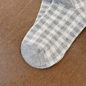 Detail of grey and white checkered knit socks with reinforced toe on wooden background