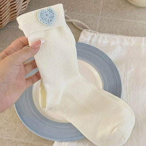 Detail of white ribbed crew sock with a light blue crocheted heart on the folded cuff