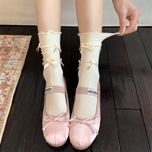 Pink satin ballet flats with bow straps and ruffled cream socks on a vintage rug