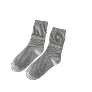 Grey knit ballet style socks with white bow and silver heart pendant on white background