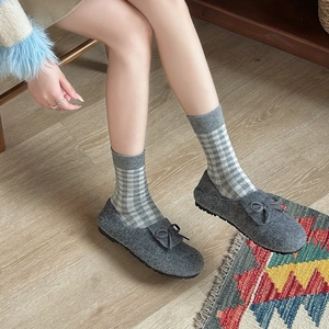 Retro plaid socks paired with grey felt bow slippers on a wooden floor, 45-degree angle