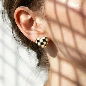 Macro shot of heart-shaped checkerboard earring with gold edging on model