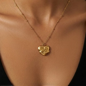 Close-up of a gold heart pendant with a ribbon design and beaded chain on a neck