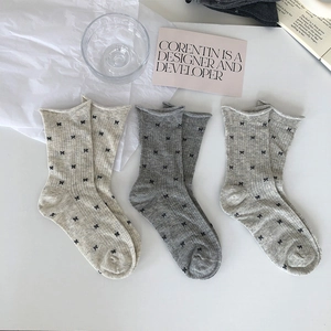 Detailed view of three pairs of grey and white socks with black bow patterns and rolled cuffs