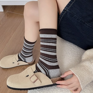Close-up of striped cotton socks paired with beige suede cork slippers on wood floor