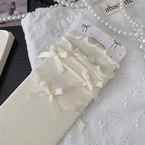 Detail of cream balletcore socks featuring delicate satin bows and wavy lace edges