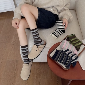 Close-up of striped cotton socks in various colors paired with beige mule shoes on sofa