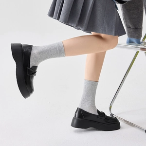 Close-up of black platform loafers with bow detail styled with white socks and a skirt